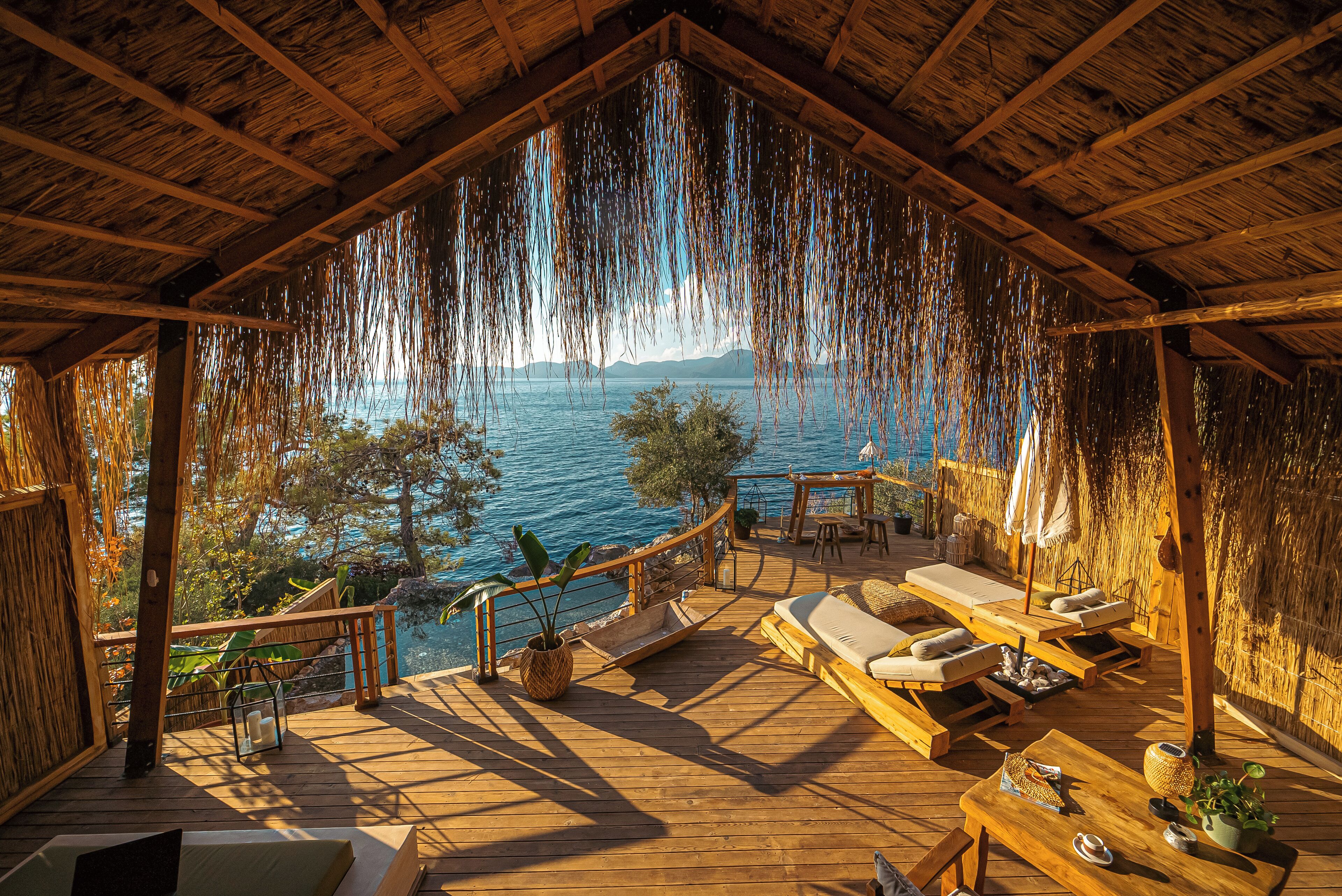 A wooden deck with lounge chairs and tables overlooking a body of water.