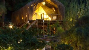 A rustic treehouse with a thatched roof, wooden deck, and a warm interior light. - Perdue Hotel (Fethiye)
