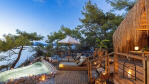 A wooden deck with a stone wall, a pool, and a lounge area with a canopy. - Perdue Hotel (Fethiye)