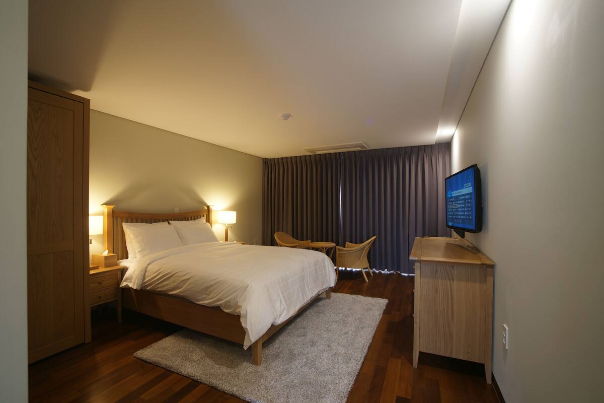 A hotel room with a wooden bed, a TV, a desk, and a chair.