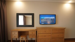 A wooden desk with drawers and a stool, a mirror, and a TV mounted on the wall. - IlleInn Hotel (Seogwipo)