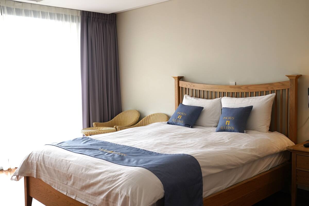 A neatly made bed with a wooden headboard, two pillows, a bedside table with a lamp, and a chair.