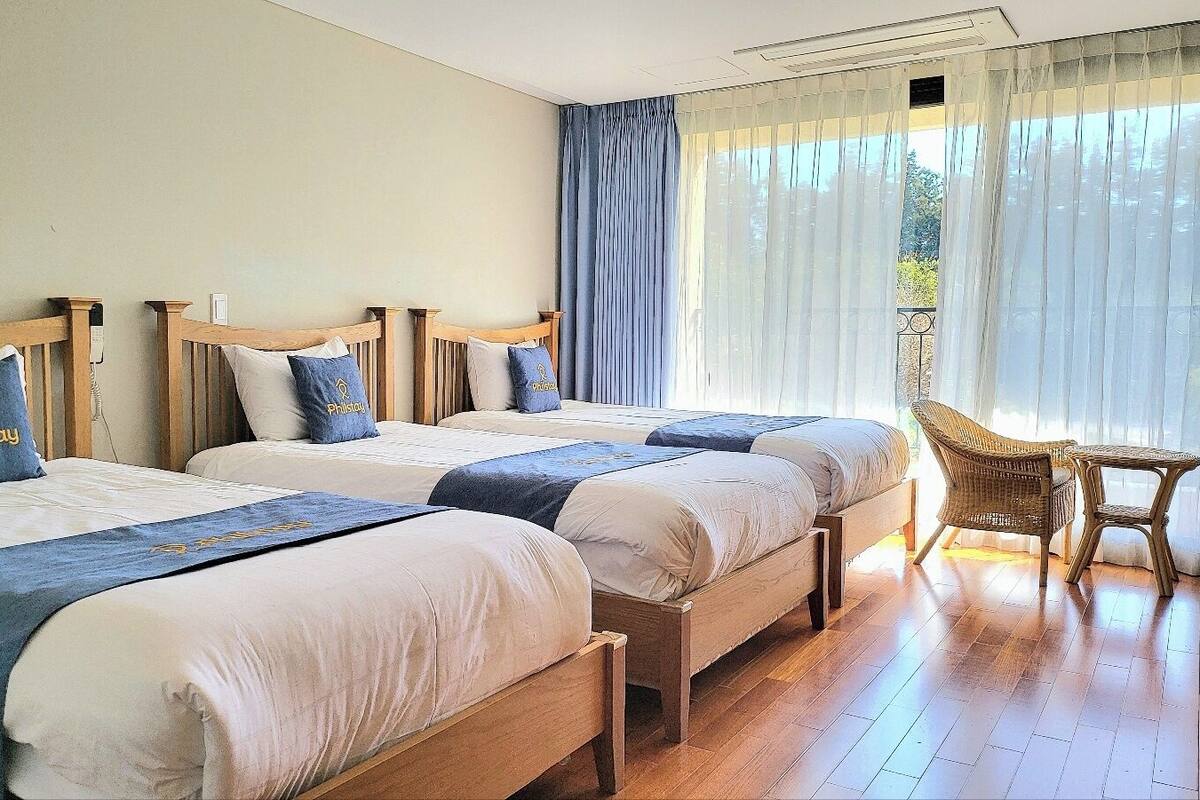 A hotel room with three wooden beds, a wicker chair, and a small table.