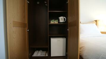 Een houten garderobekast met een geïntegreerde minibar, planken en een schoenenrek.