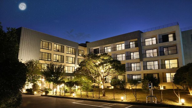 A multi-story hotel with illuminated windows and a parking lot. - IlleInn Hotel (Seogwipo)