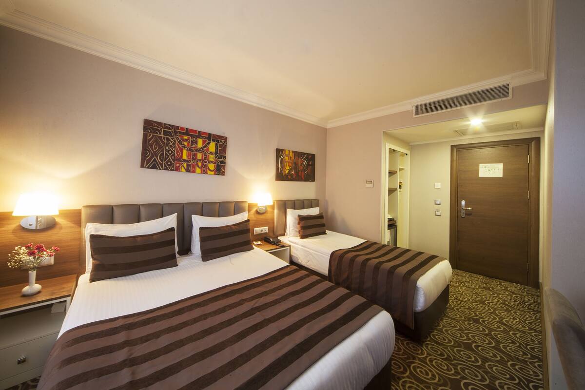 Habitación de hotel con dos camas, una mesita de noche con lámpara y cuadros en las paredes.