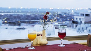 Una mesa con dos vasos de bebidas, un florero con flores y vista a un paisaje urbano desde la ventana.