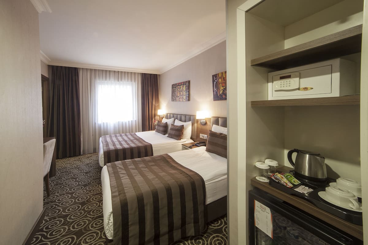 Una habitación de hotel con dos camas, un minibar, una cafetera y un ventanal con cortinas.