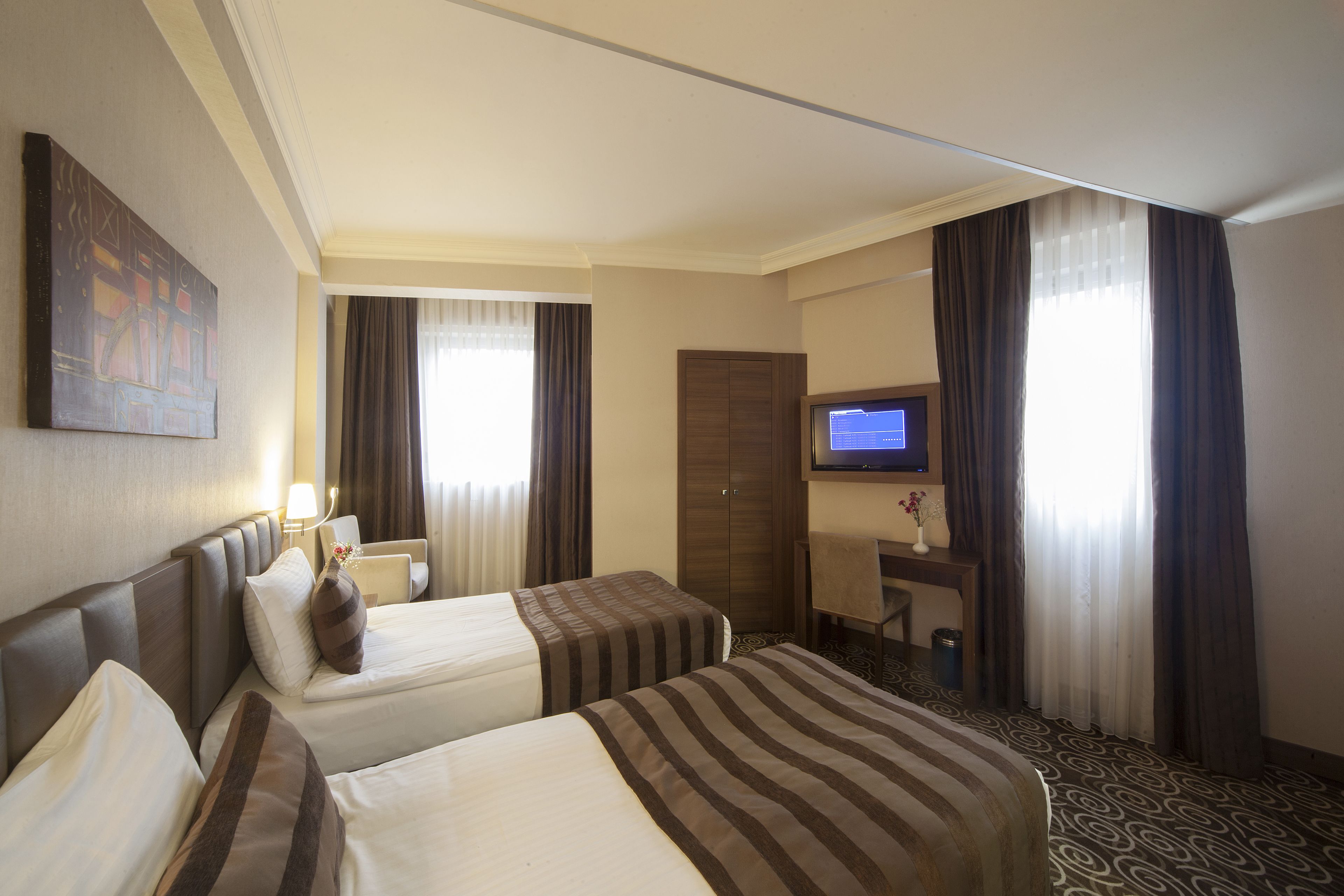 A hotel room with two beds, a desk, a television, and a window with curtains.