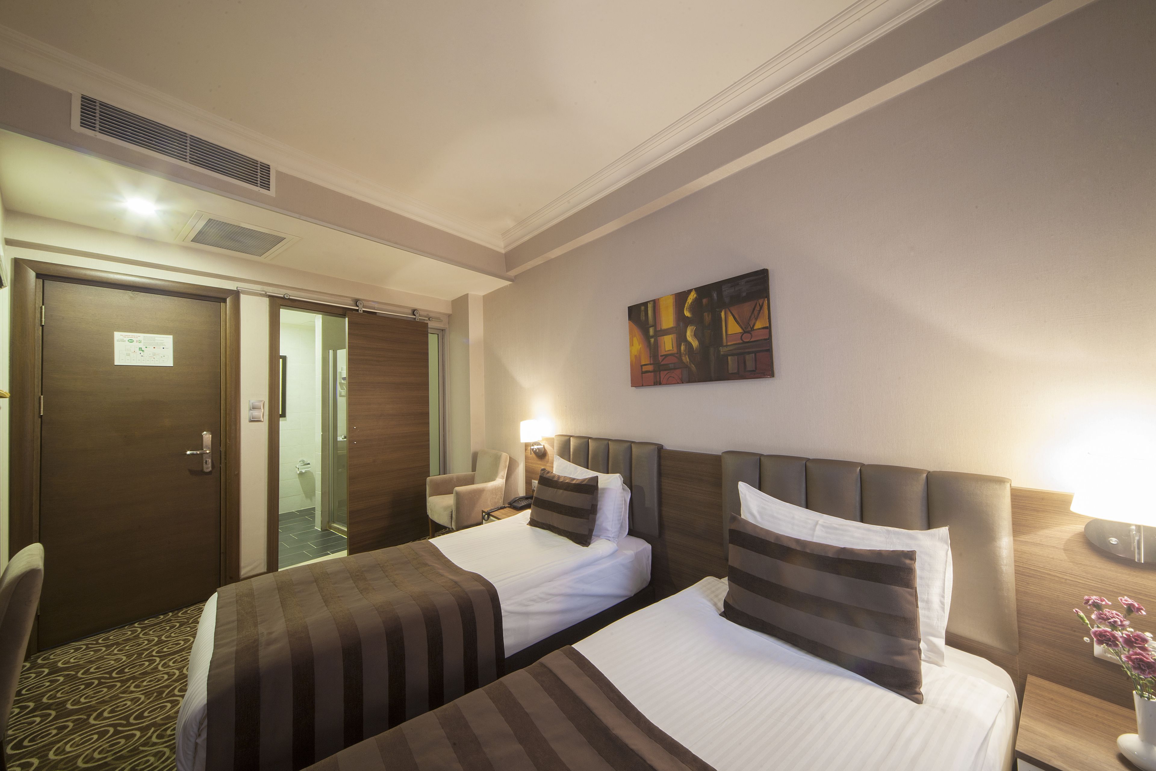 A hotel room with two beds, a chair, a nightstand, and a painting on the wall.