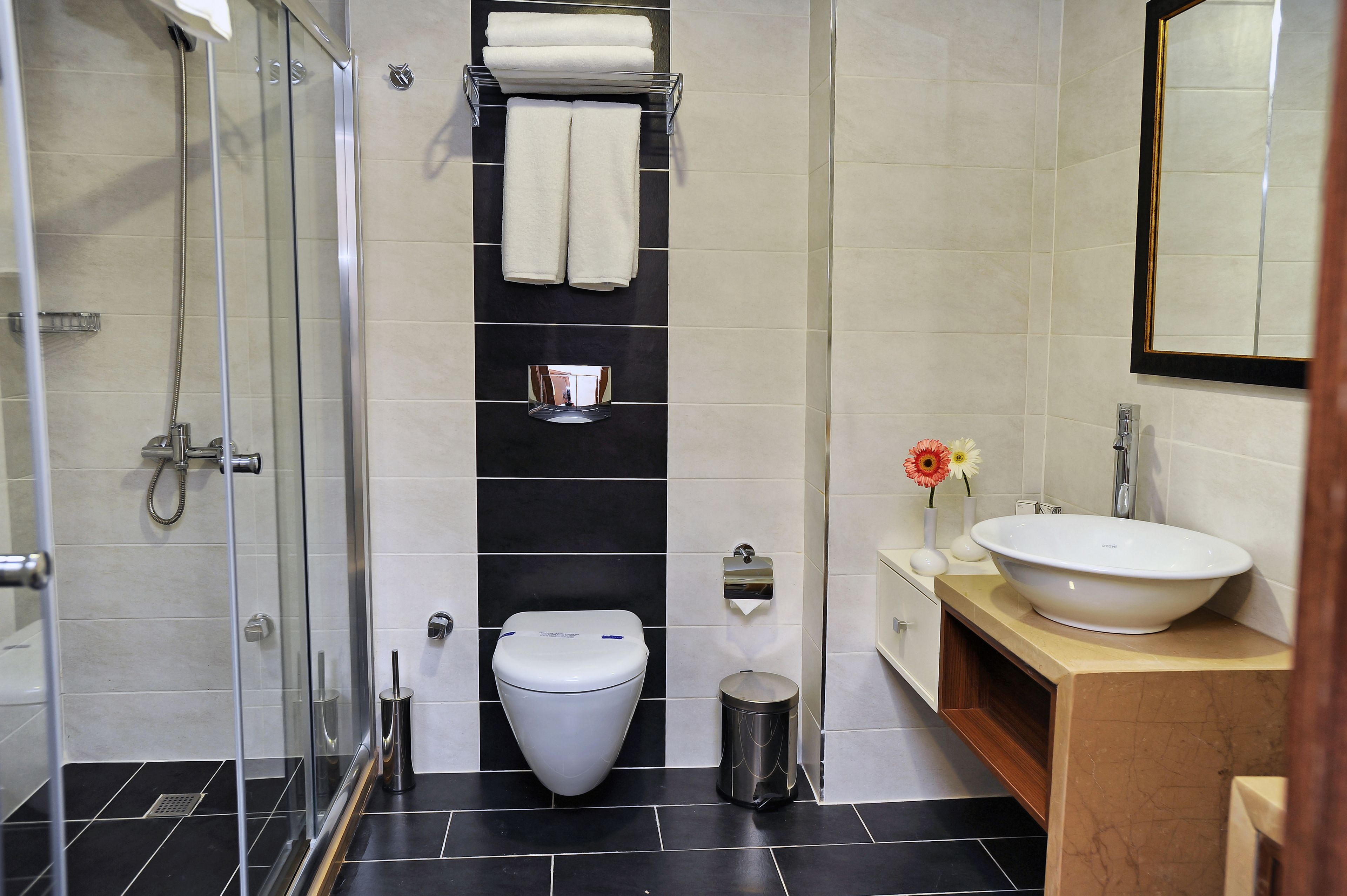 A modern bathroom with a glass-enclosed shower, a white toilet, and a sink with a vase of flowers.