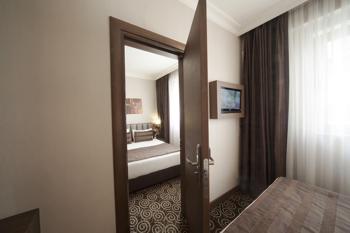 Una habitación de hotel con una cama, un televisor montado en la pared y una puerta que da a otra habitación.