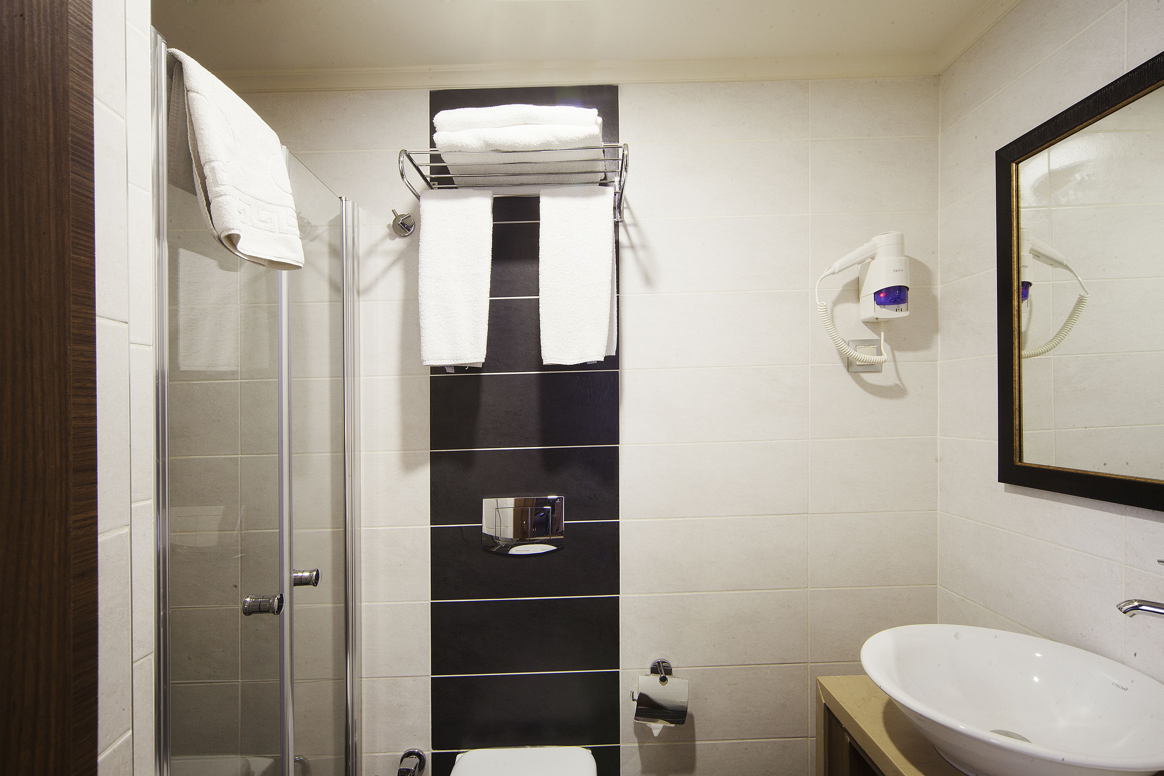 A bathroom with a glass shower enclosure, a white sink, and a towel rack with two towels.