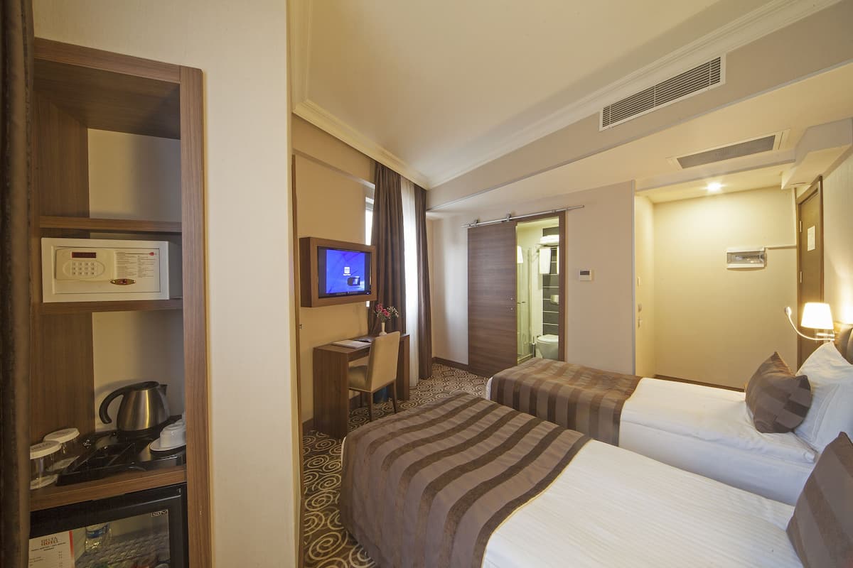 Habitación de hotel con dos camas, un escritorio con televisor, kitchenette y baño.