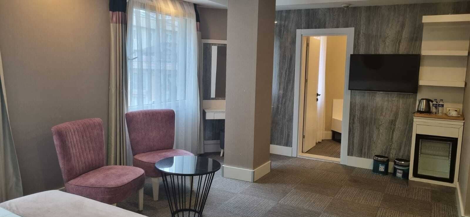 A hotel room with a seating area, a small table, a TV, and a kitchenette.