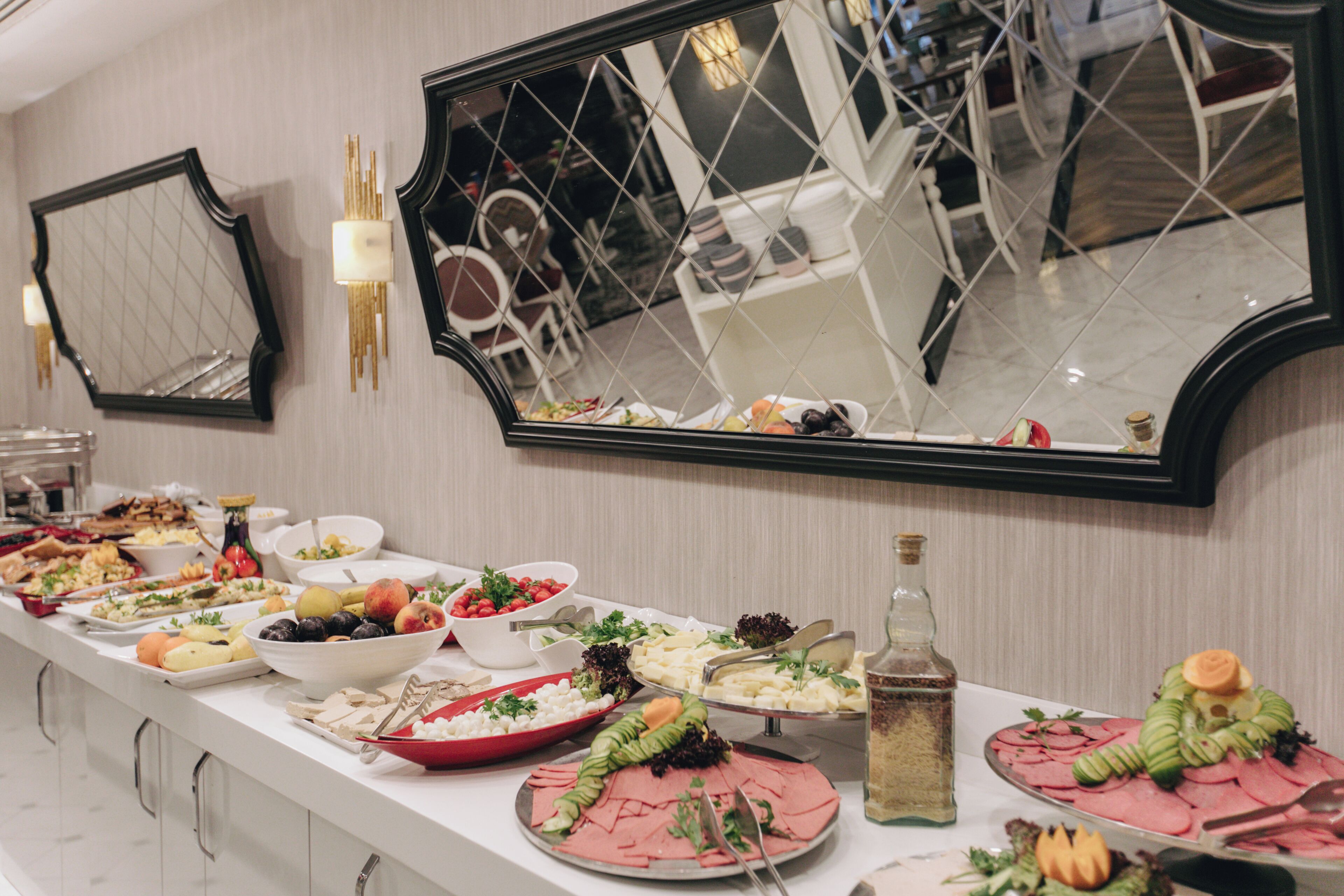 A buffet table with various dishes, a large mirror, and a bottle of olive oil.