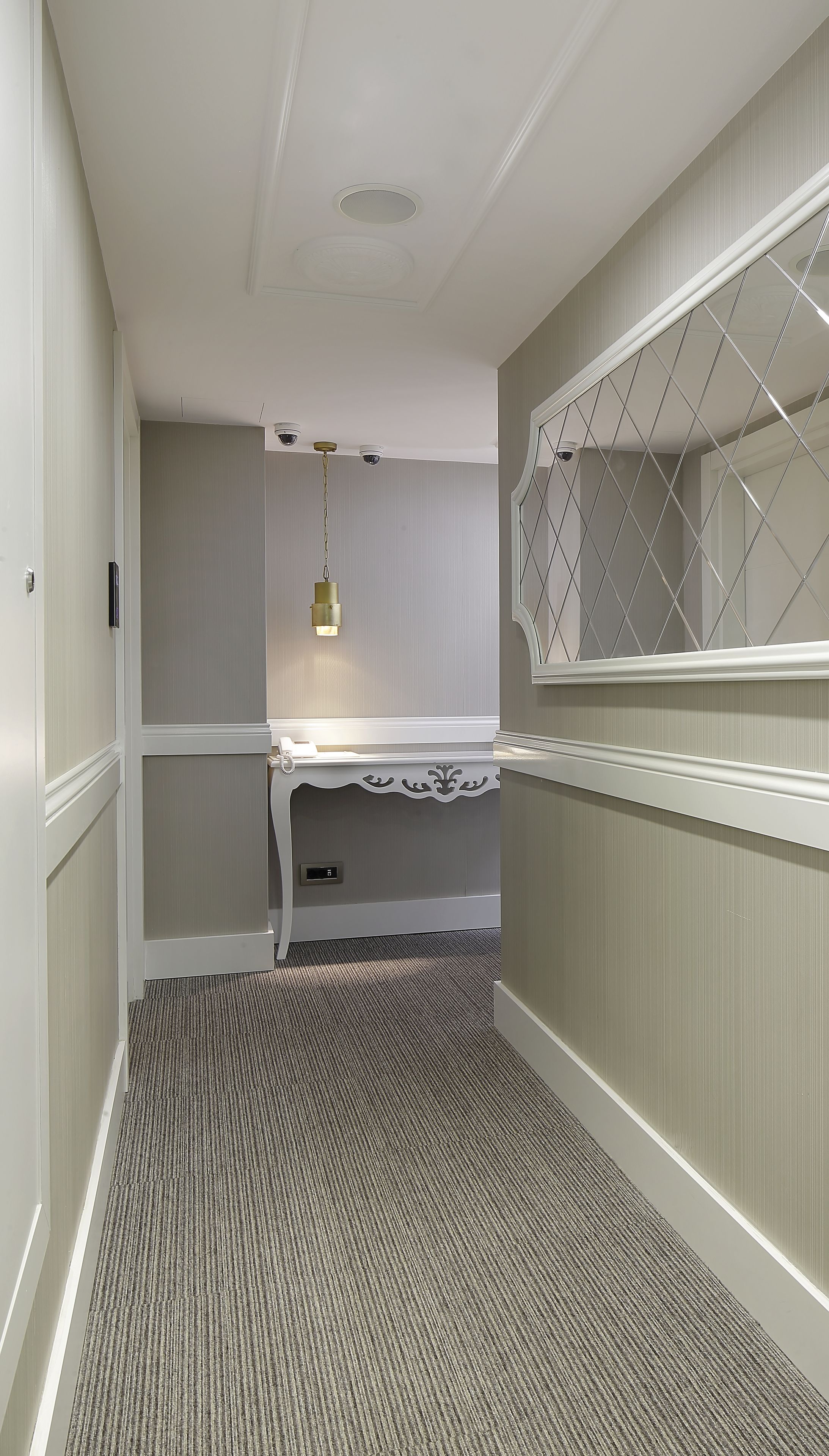 A narrow hallway with a carpeted floor, a white door on the left, and a window with a diamond-patterned blind on the right.