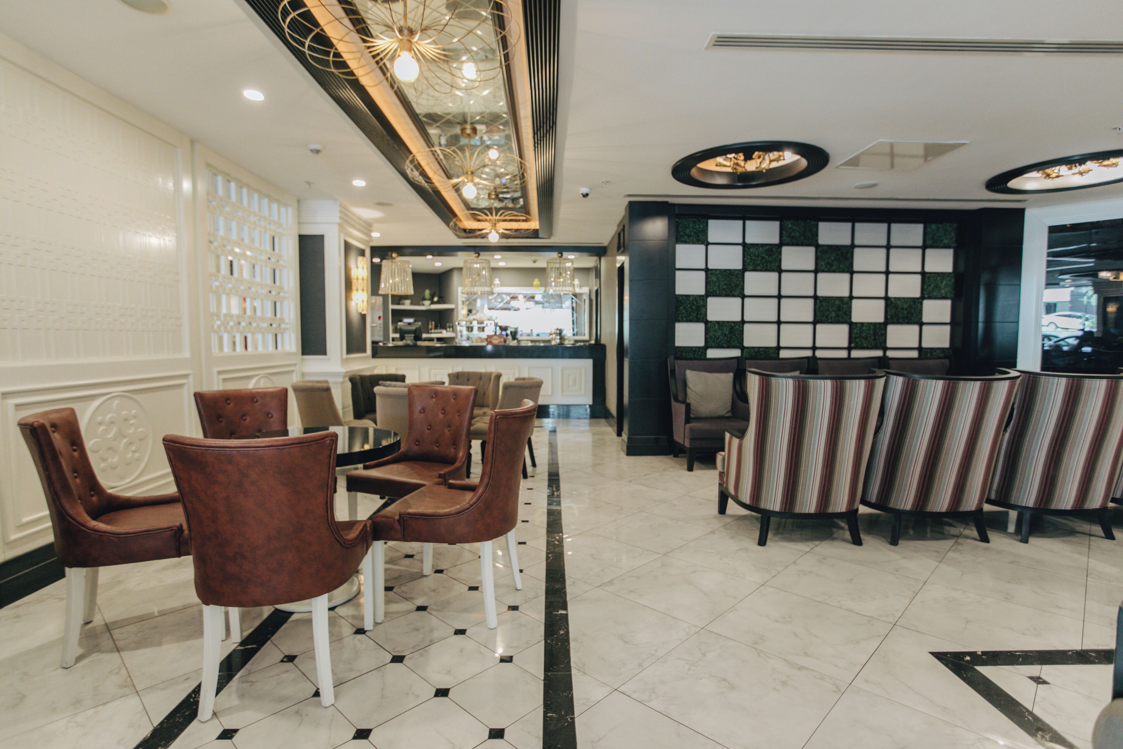 A hotel lobby with a dining area featuring brown upholstered chairs and a bar area with striped chairs.