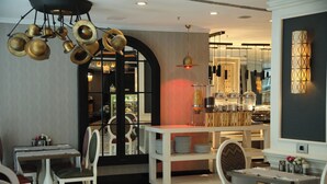 Un espace repas avec des tables et des chaises blanches, un chariot de service central et un lustre décoratif.