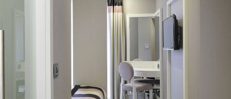 A hotel room with a bed, a desk, a chair, a television, and a mirror.