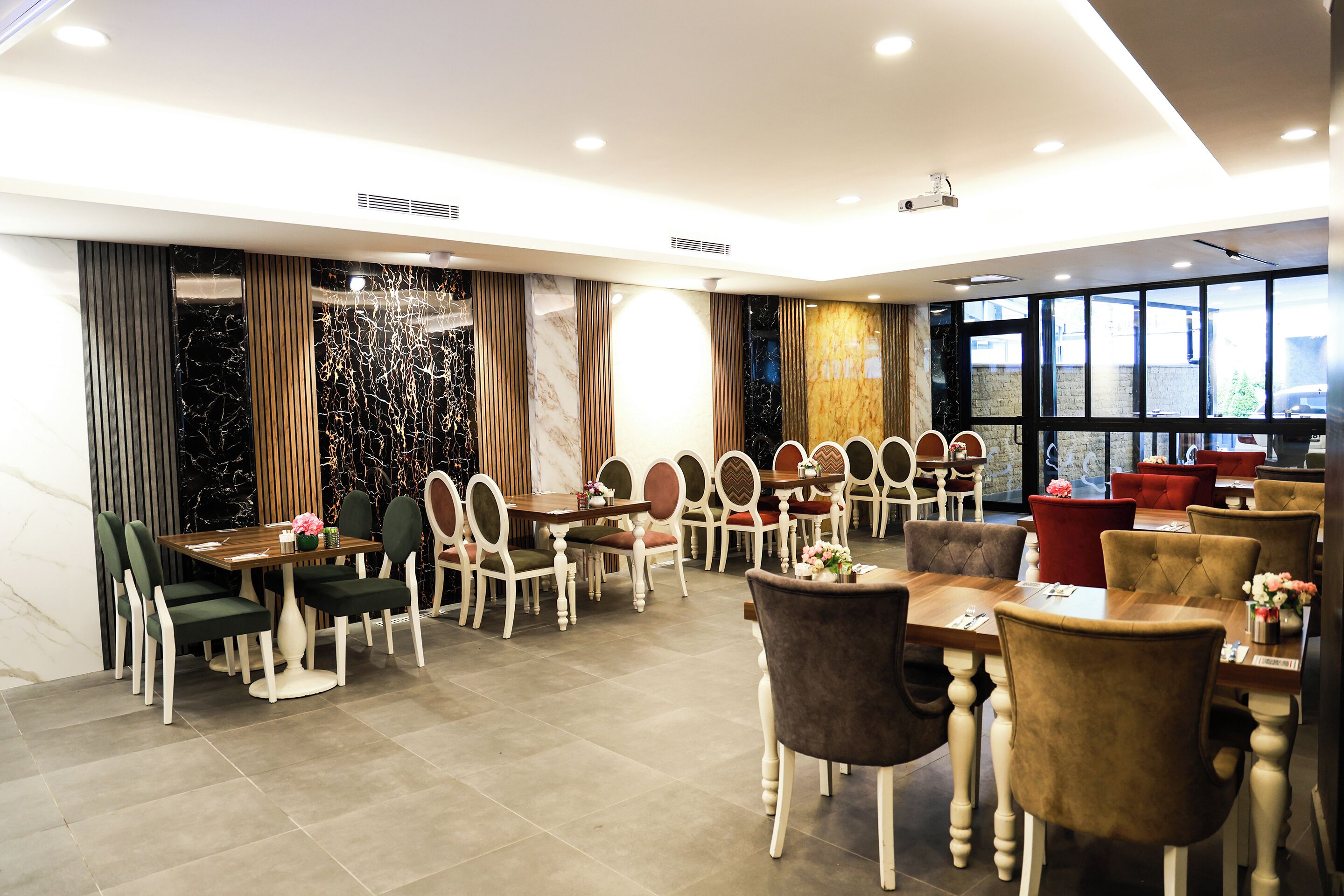 A modern dining area with multiple tables and chairs, large windows, and a decorative wall.