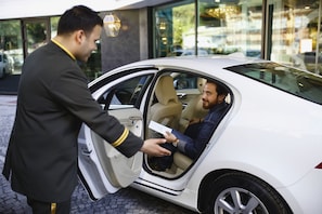 A white car with its door open, a man handing a card to a seated woman inside. - Mia Berre Hotels (Istanbul)