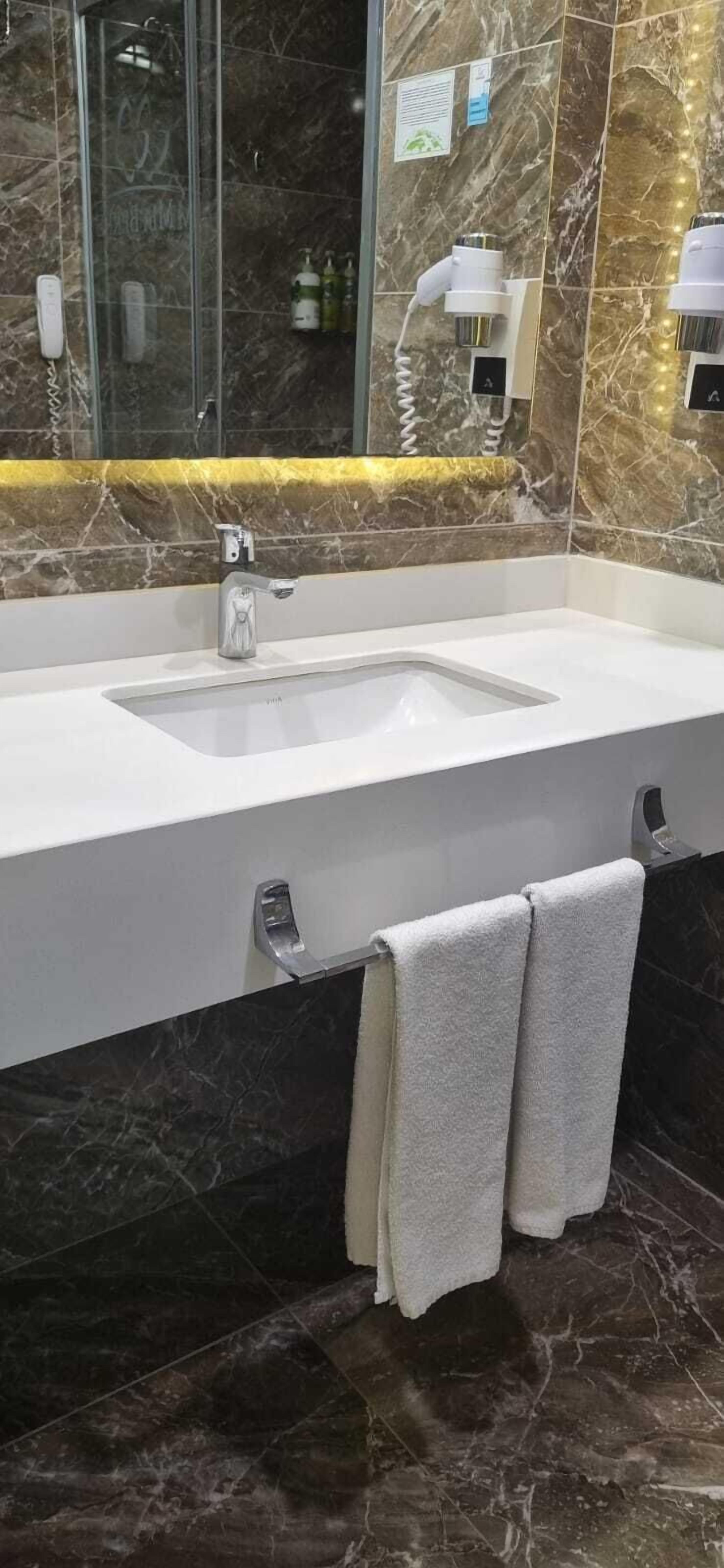 A bathroom with a marble sink, a mirror, and a towel rack.