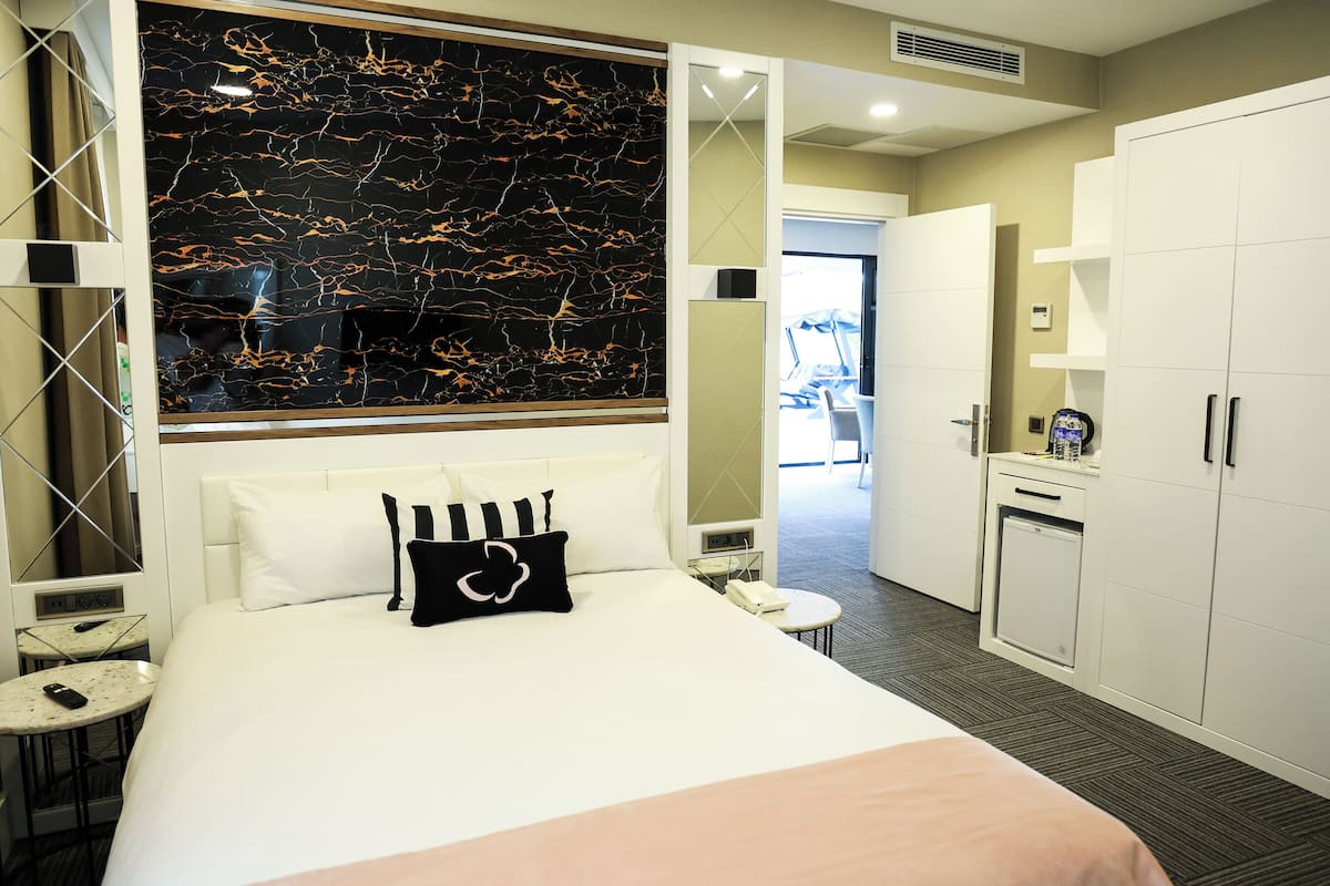 A hotel room with a large bed, a small bedside table, a desk, a wardrobe, and a bathroom visible through an open door.