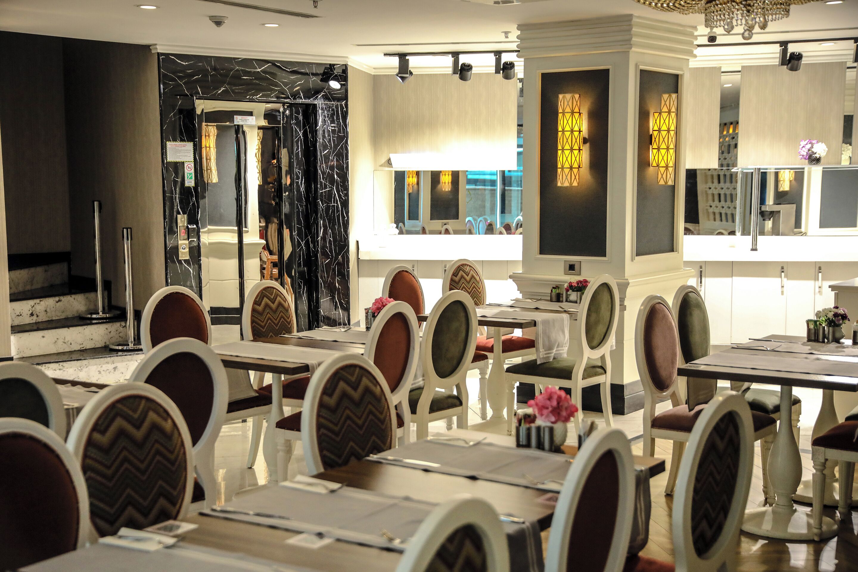 A restaurant with white tables and chairs, a chandelier, and a view of the street.
