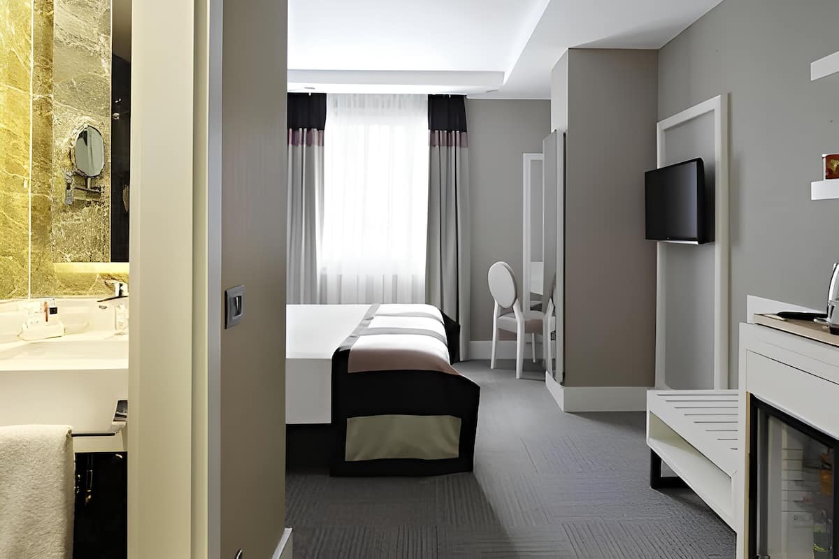 A hotel room with a bed, a TV, a desk, and a bathroom with a mirror and sink.