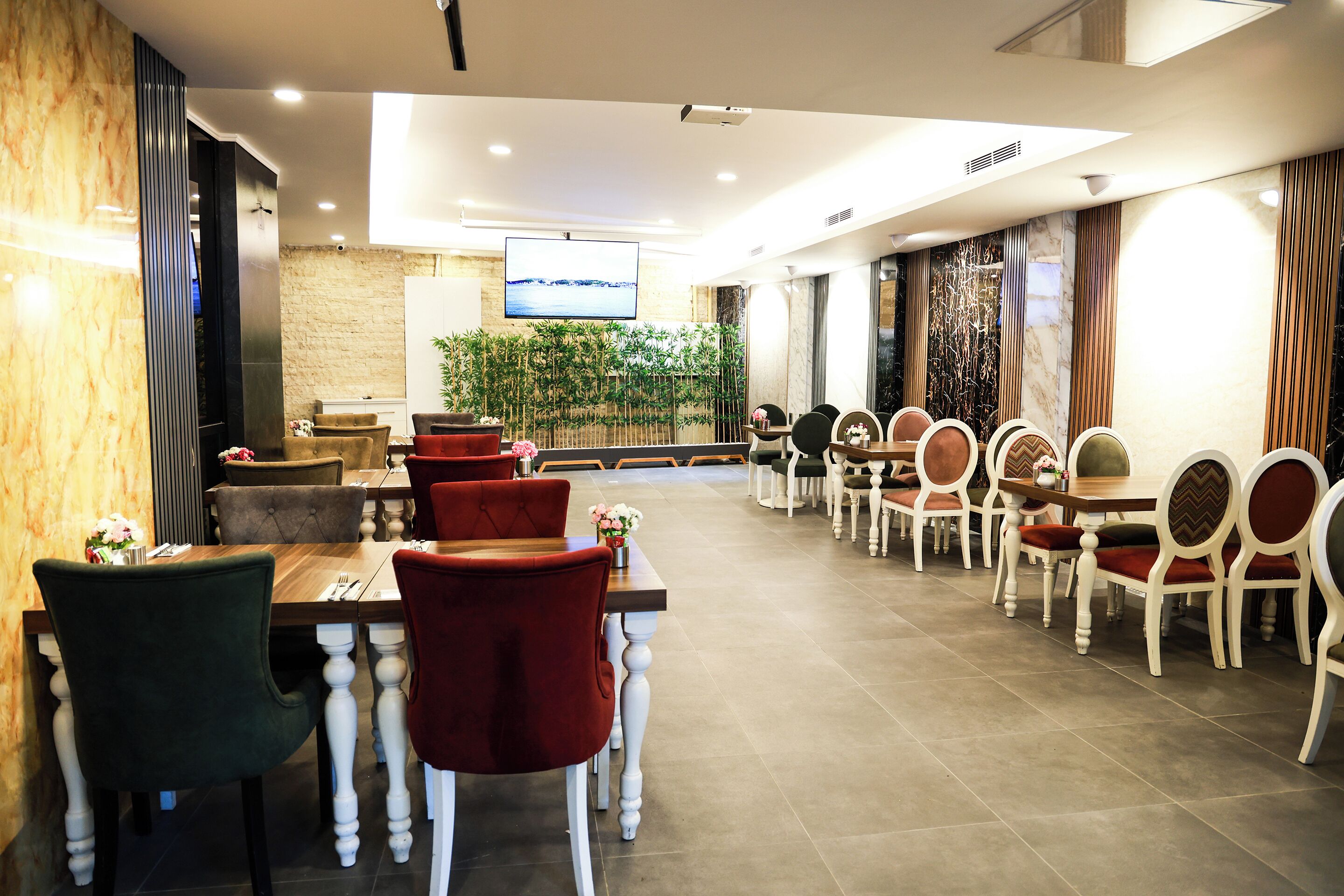 A restaurant with multiple dining tables and chairs, a television screen, and a decorative plant wall.