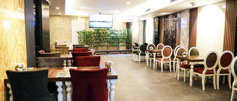 A restaurant with multiple dining tables and chairs, a television screen, and a decorative plant wall.