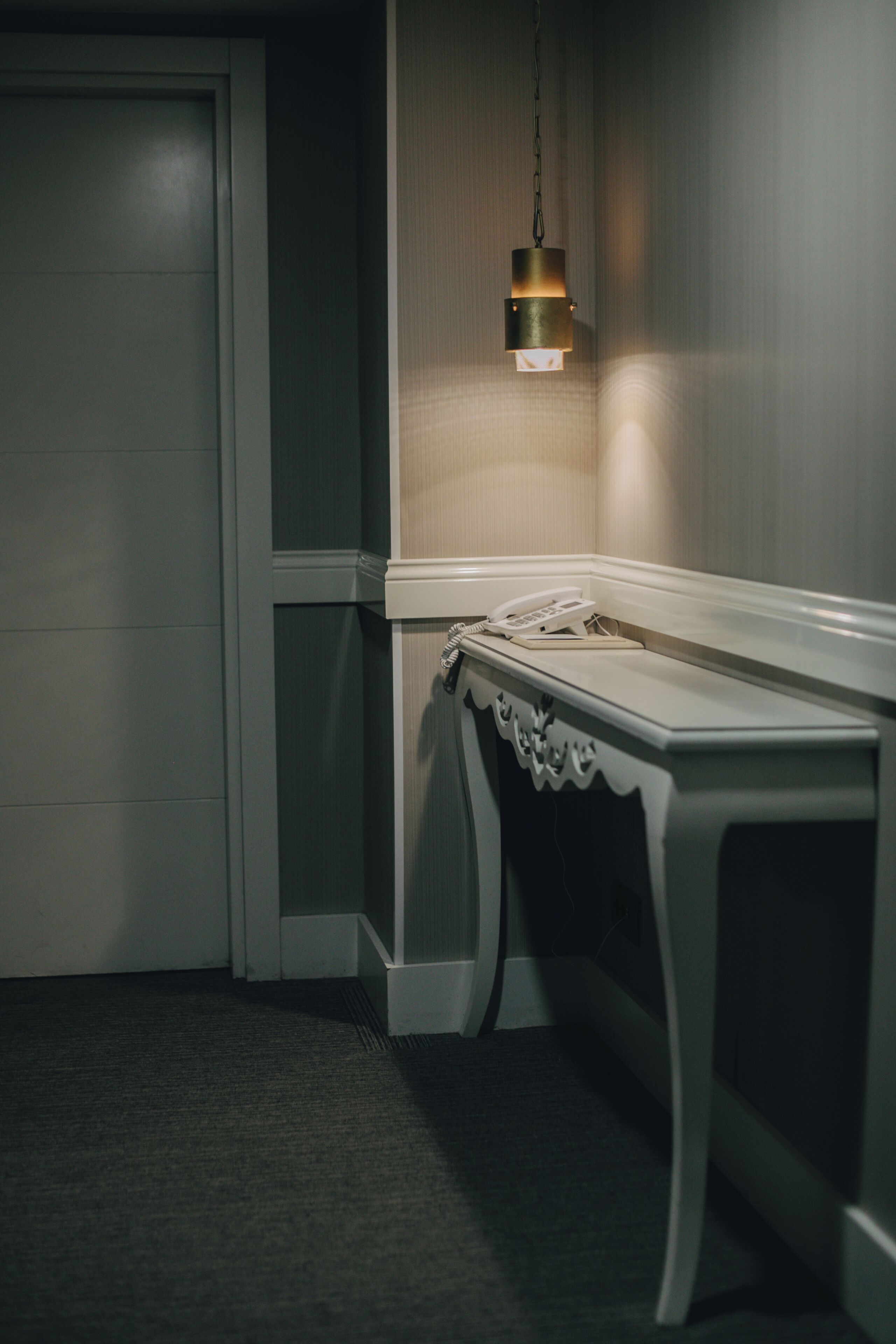 Habitación de hotel con puerta cerrada, mesita de noche con teléfono y lámpara de pared.