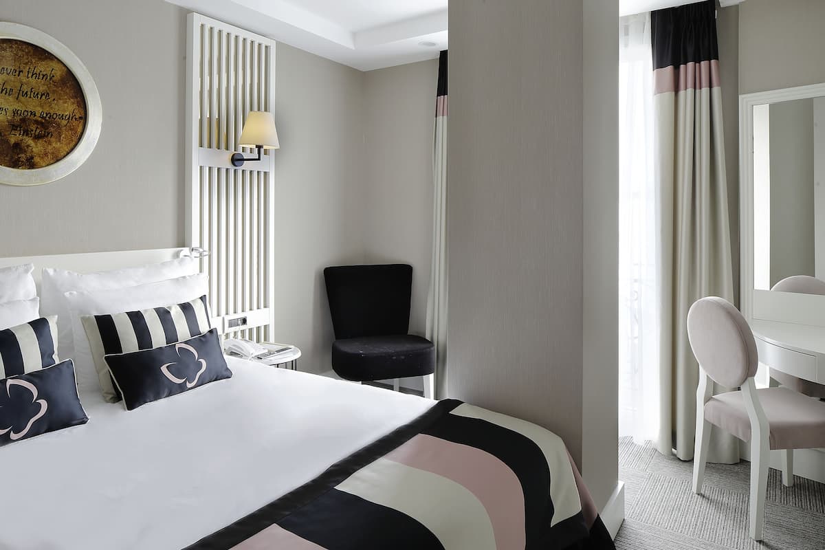A hotel room with a bed, a desk, a chair, a lamp, and a window with curtains.