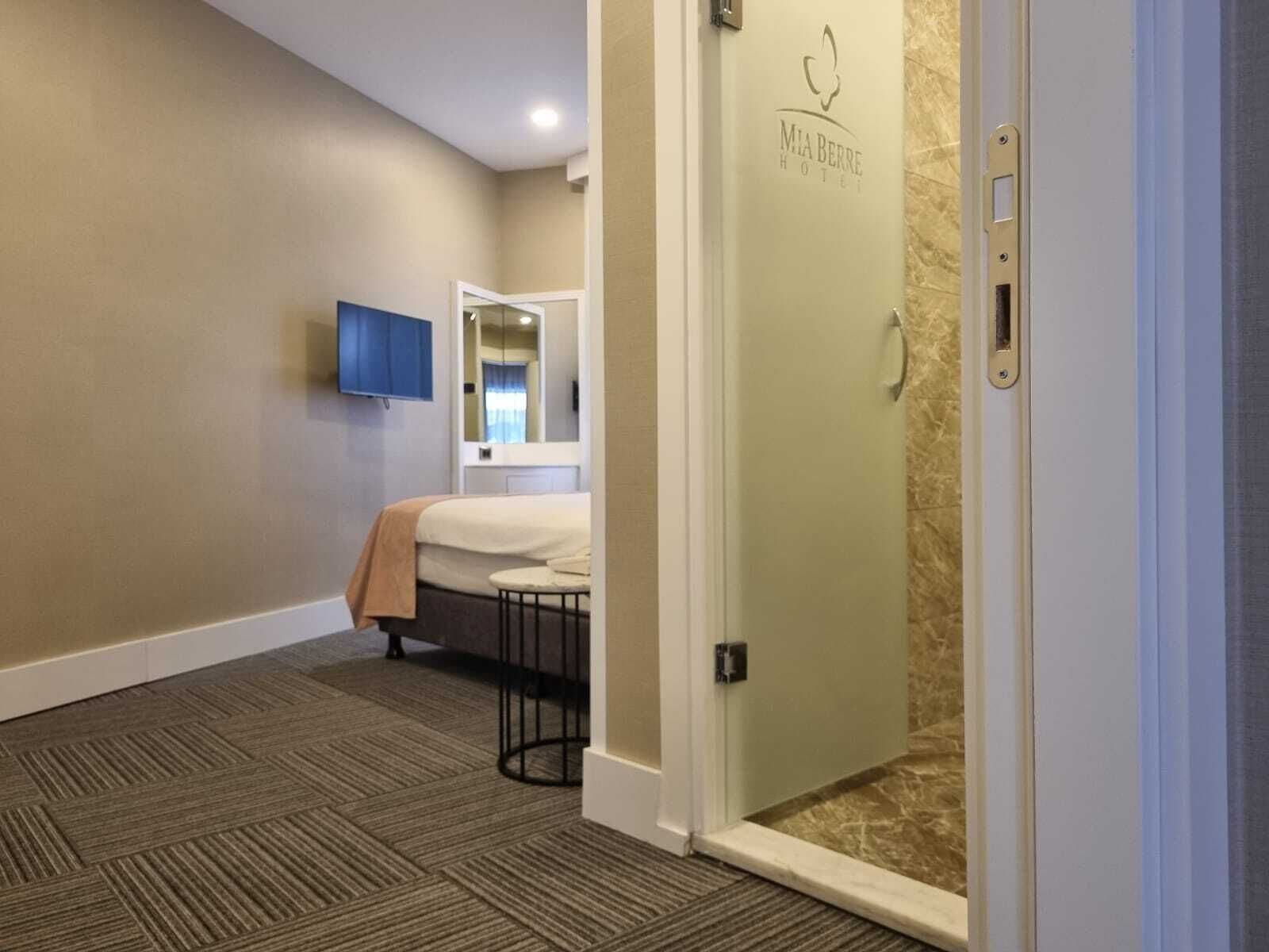A hotel room with a bed, a small table, a TV mounted on the wall, and a shower area.