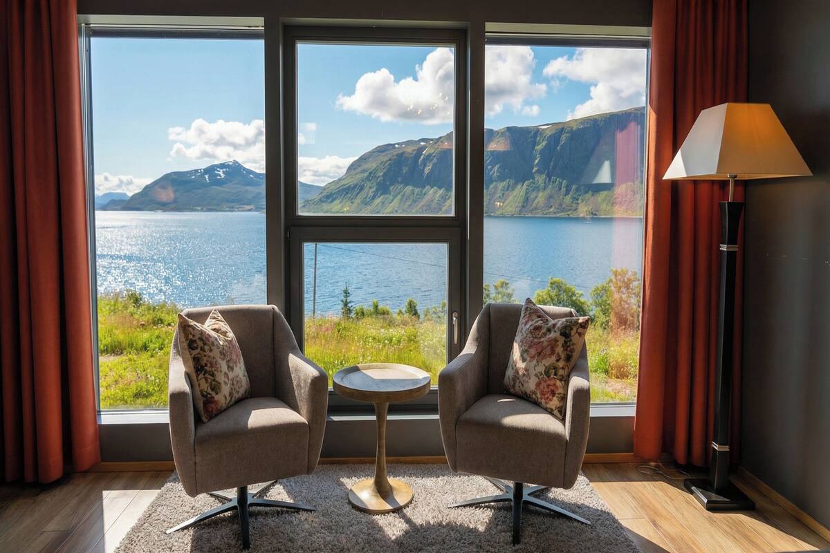 Une pièce avec deux fauteuils placés face à une grande fenêtre donnant sur un lac et des montagnes.