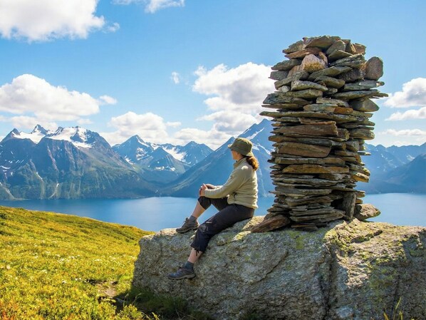A person sitting on a rock with a stone wall and a mountainous landscape in the background. - Arctic Panorama Lodge (Skjervoy)