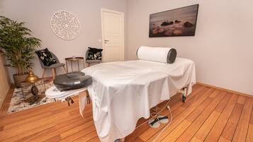 Relax in this serene space with a massage table, black massage chair, and a calming potted plant.