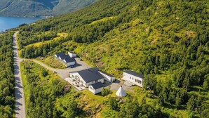 A remote, mountainous area with a small cluster of white buildings surrounded by dense forests and a lake. - Arctic Panorama Lodge (Skjervoy)