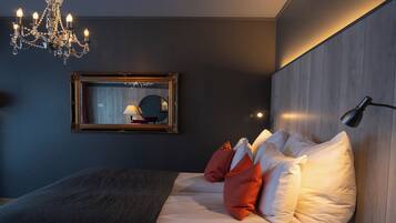 A modern bedroom with a large bed, a chandelier, a mirror, and a bedside lamp.