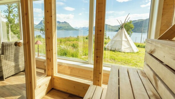 A wooden cabin with large windows overlooking a lake and mountains. - Arctic Panorama Lodge (Skjervoy)