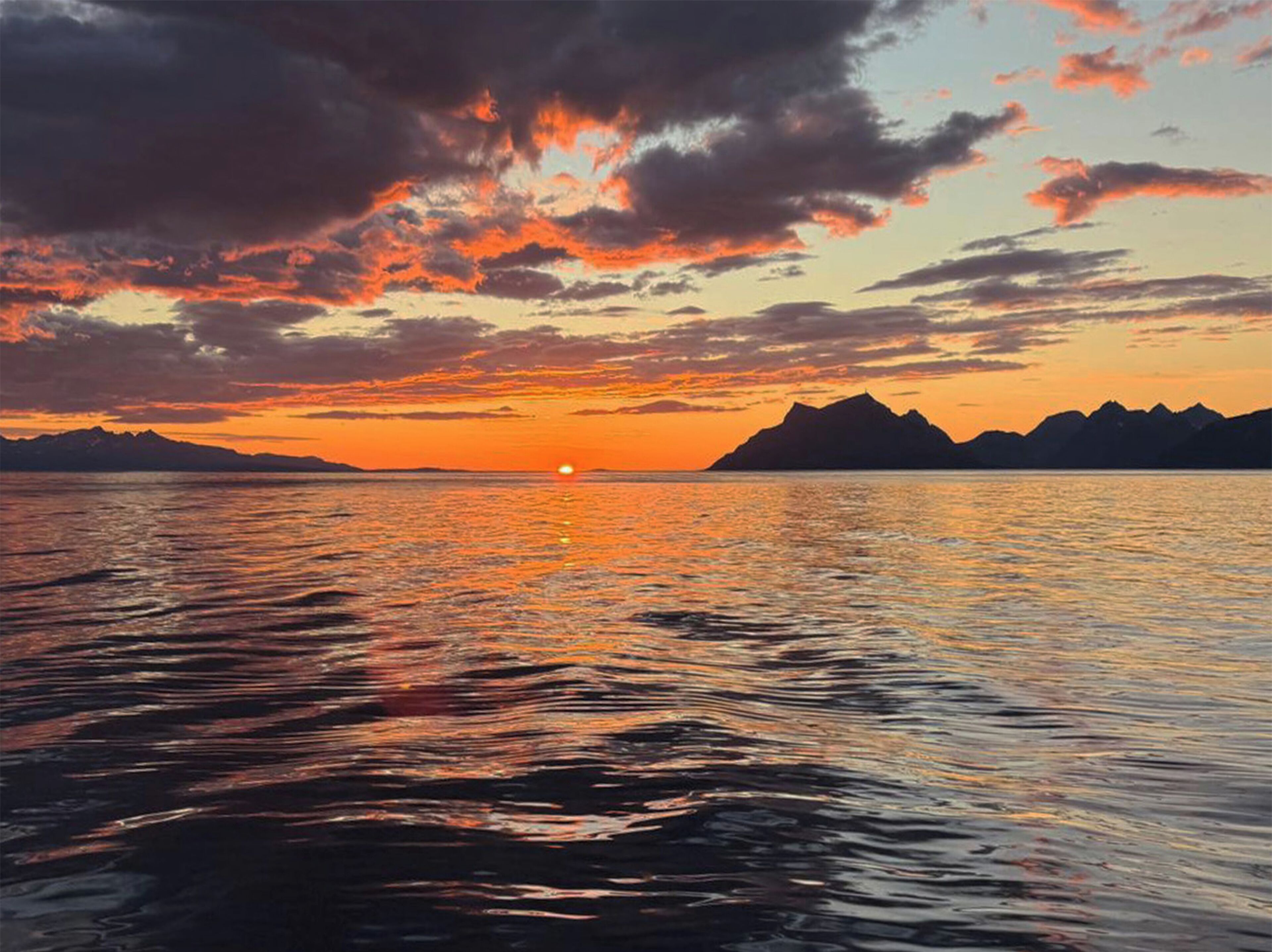 A sunset over a calm sea with mountains in the distance.