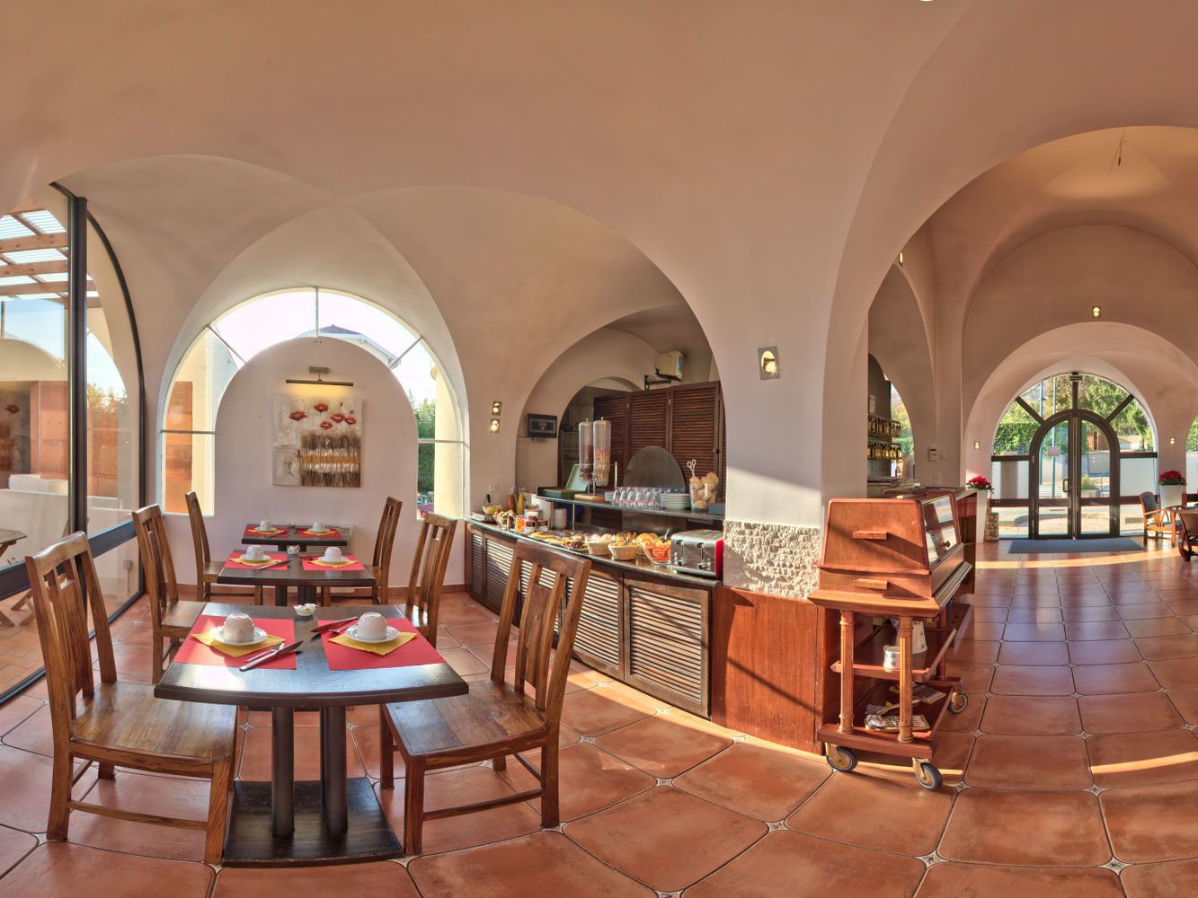 A spacious dining area with high arched ceilings, wooden tables, and chairs. A central bar area with a counter and bar stools is visible.