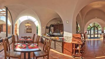 A spacious dining area with high arched ceilings, wooden tables, and chairs. A central bar area with a counter and bar stools is visible.