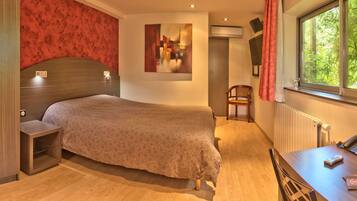 Un dormitorio con cama, mesitas de noche, una silla, una mesa y una ventana con cortinas.