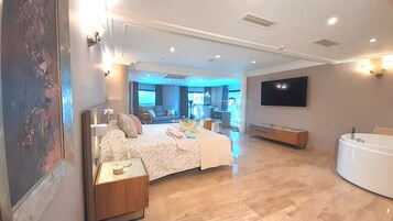 Un dormitorio moderno con una cama grande, mesitas de noche, televisión y un baño independiente con bañera.