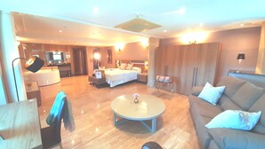 Ein modernes Hotelzimmer mit einem Bett, einer Sitzecke mit Couchtisch, einer Couch und einem Schreibtisch mit Stuhl.