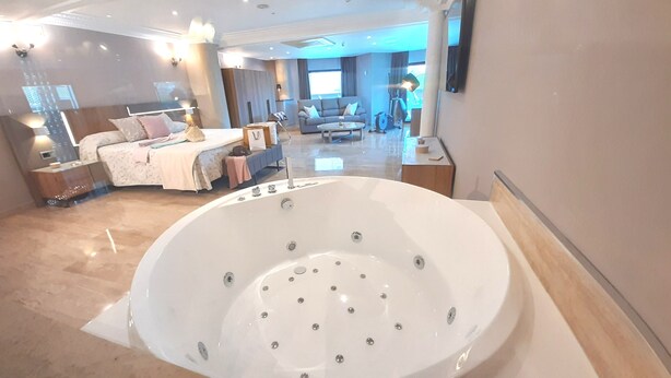 Ein geräumiges Schlafzimmer mit einer großen Badewanne, einem Sofa und einem Essbereich im Hintergrund.