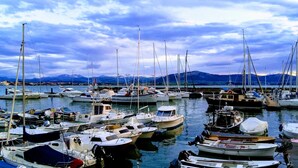 Ein Yachthafen mit verschiedenen Schiffen, ruhigem Wasser und Bergen im Hintergrund.