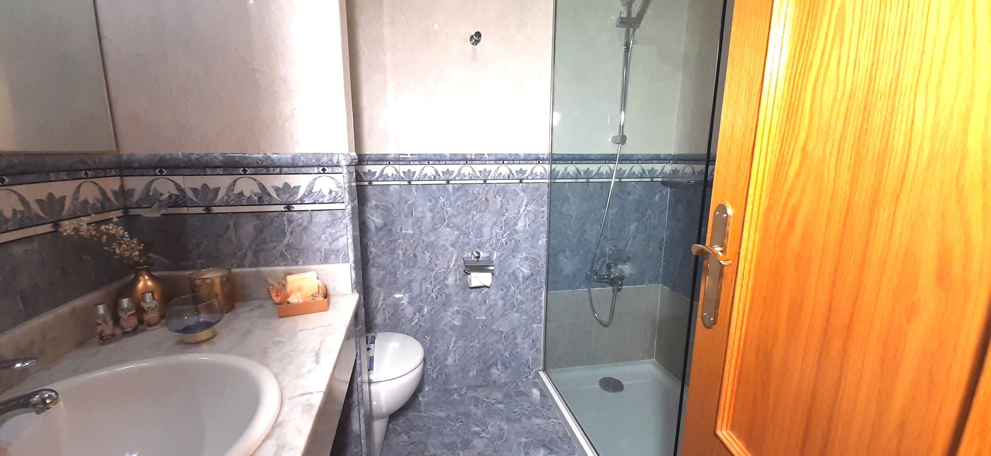 A bathroom with a marble sink, a toilet, and a glass-enclosed shower.